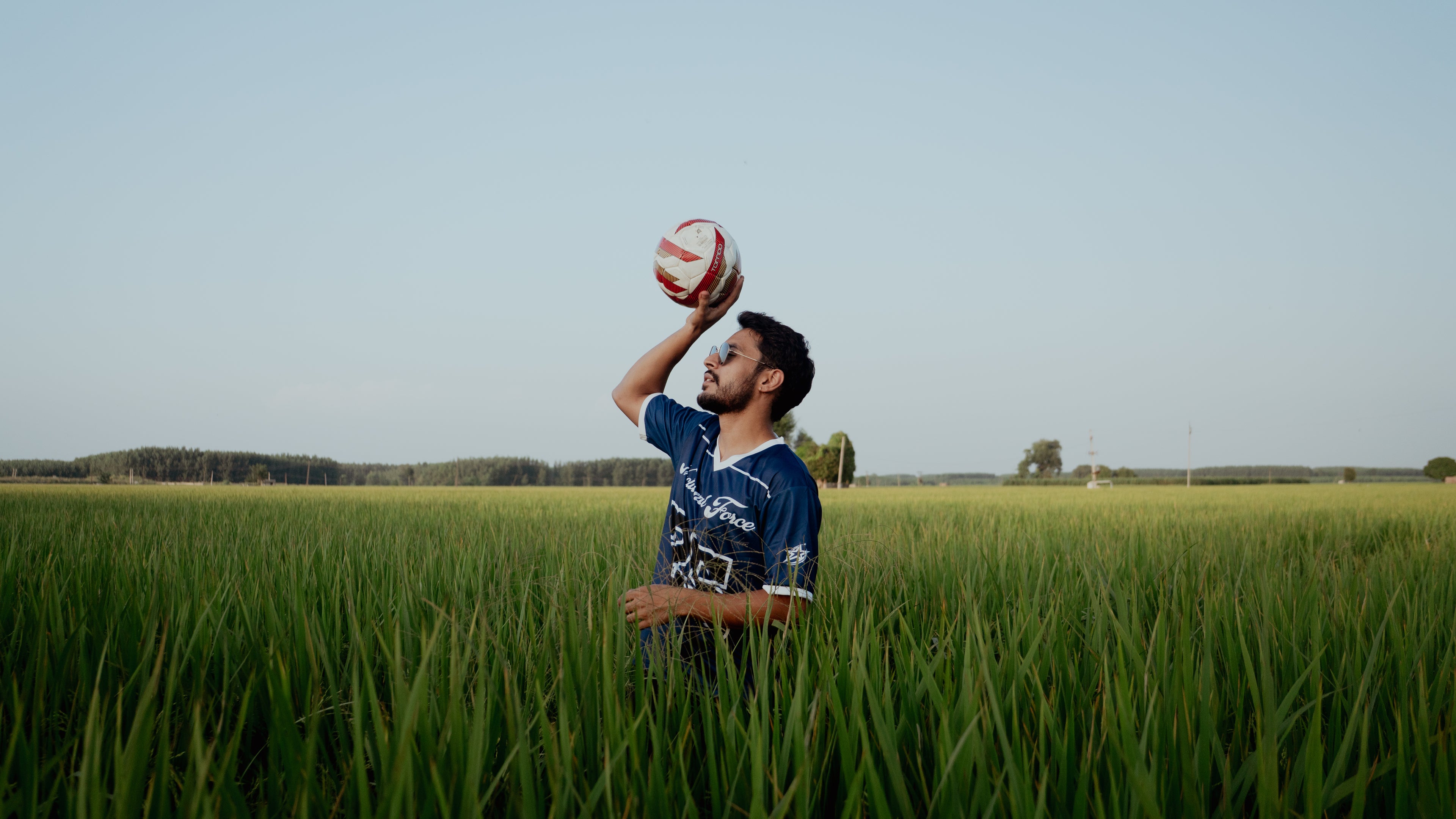Man holding a soccer ball in a grassy field with a clear sky